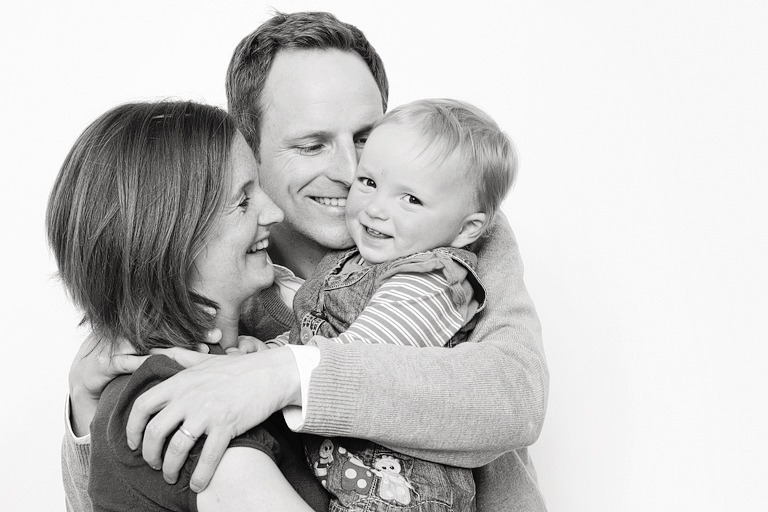 family cuddling in black and white, baby is smiling at the camera