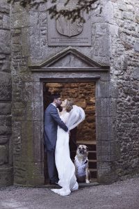 wedding couple kissing in a derelict castle with their dog at their feet