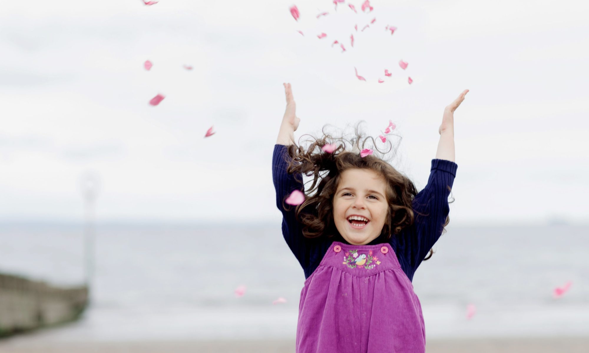 little girl throwing pink confetti into the air on grey day on a beach