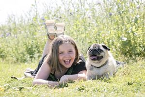 girl with pet pug laying in a field of wild flowers.