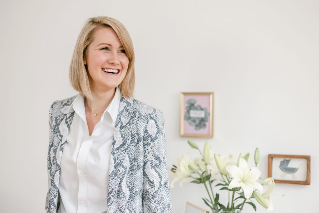 woman wearing a grey blazer and white shirt laughing out of camera