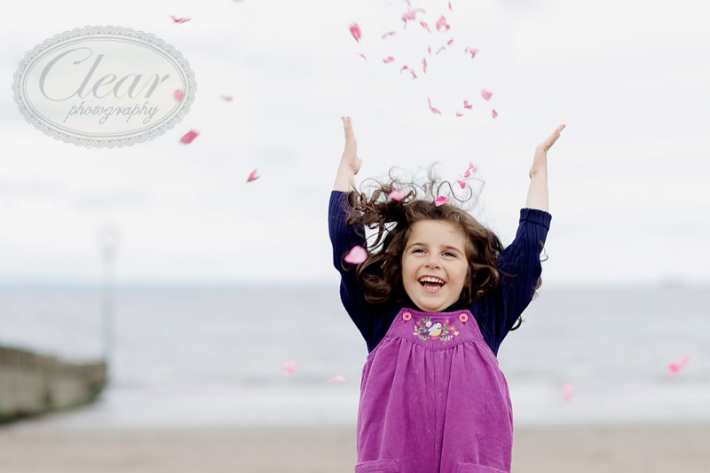 child throwing pink confetti in the air on the beach