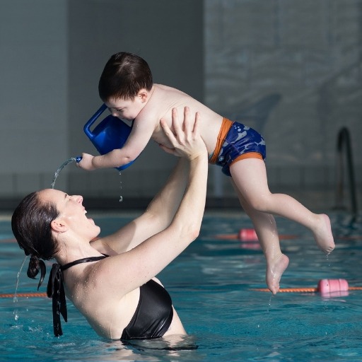 mother and son in swimming pool, son is pouring water on his mum with a watering can